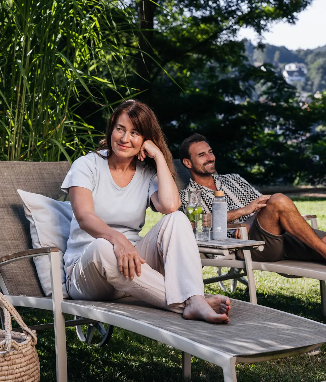Eine Frau und ein Mann sitzen auf zwei Liegen umgeben von Natur
