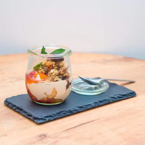 Eine Süßspeise aus Früchten und Nüssen stehen auf einem Serviebrett mit eine Löffel in einem Glas
