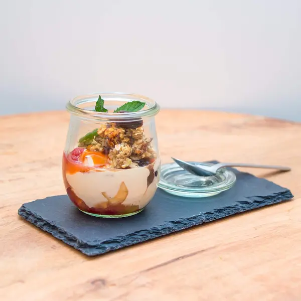 Eine Süßspeise aus Früchten und Nüssen stehen auf einem Serviebrett mit eine Löffel in einem Glas