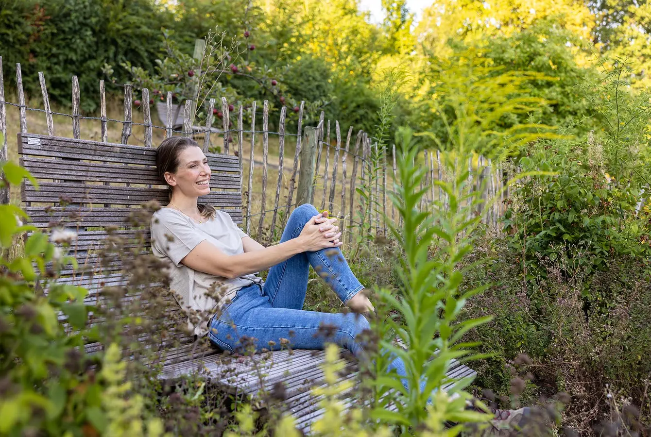 Eine Frau sitzt auf einer Parkbank im Kräutergarten der Dr. von Weckbecker Klinik und schaut in die Ferne.
