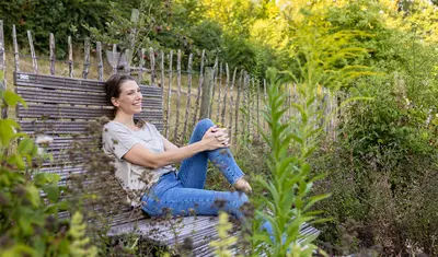 Eine Frau sitzt auf einer Parkbank im Kräutergarten der Dr. von Weckbecker Klinik und schaut in die Ferne.