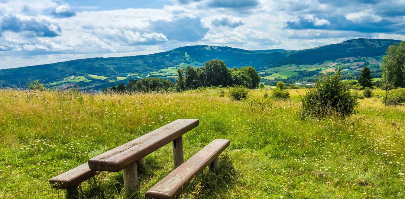 Zwei Bänke und ein Tisch auf einer Wiese in der Rhön, mit Bergen im Hintergrund