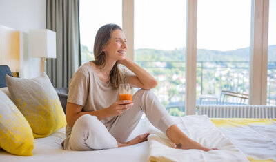 Frau sitzt auf einem Bett in der Dr. von Weckbecker Klinik mit einem Saft in der Hand