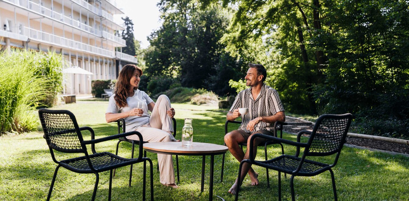 Eine Frau und ein Mann sitzen vor der Weckbeckerklinik an einem Tisch auf Gartenmöbeln