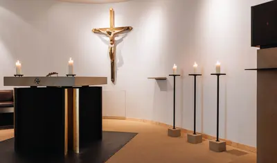 Ein Raum mit Kerzen, einem Altar und einem Jesuskreuz an der Wand