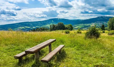 Zwei Bänke und ein Tisch auf einer Wiese in der Rhön, mit Bergen im Hintergrund