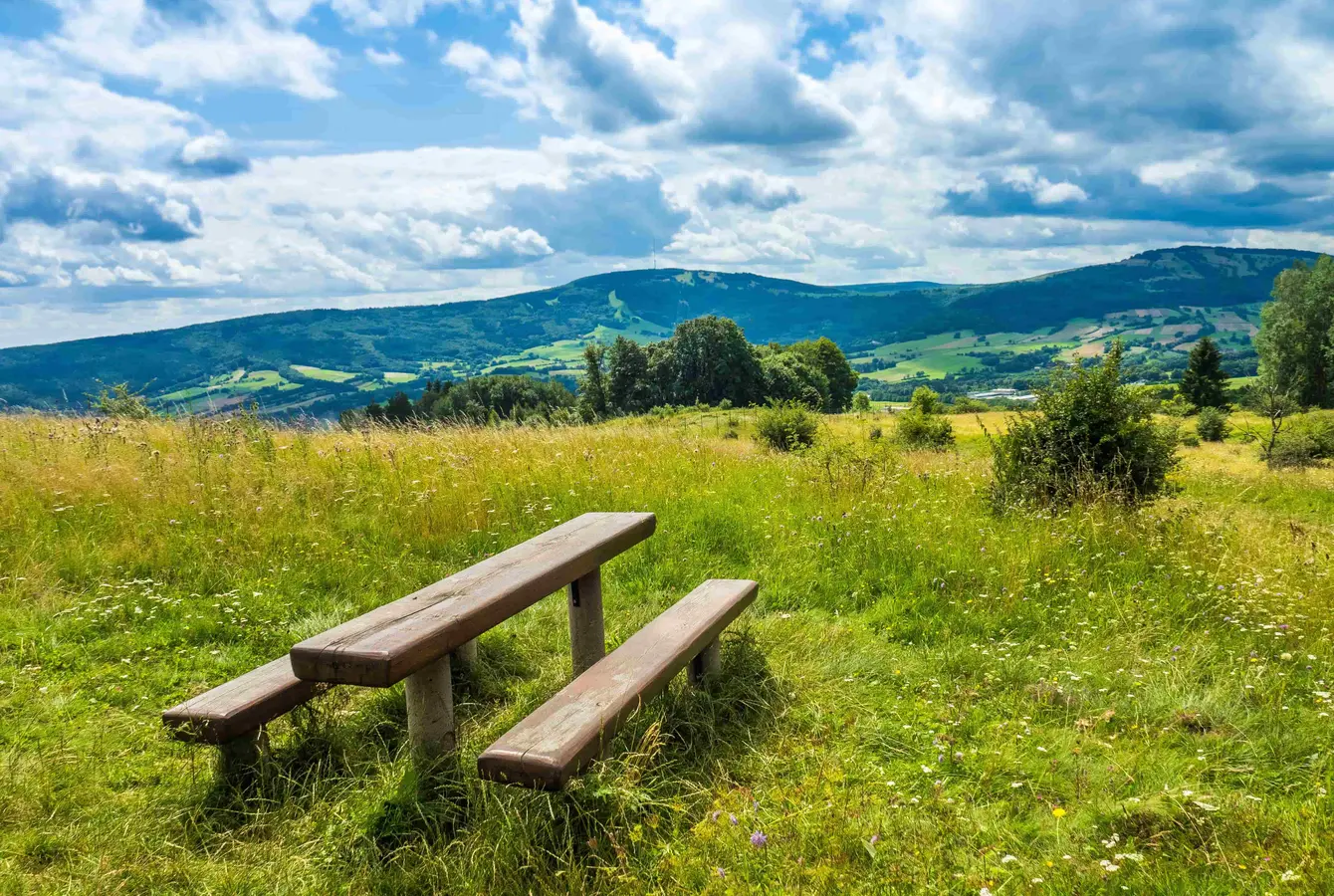 Zwei Bänke und ein Tisch auf einer Wiese in der Rhön, mit Bergen im Hintergrund