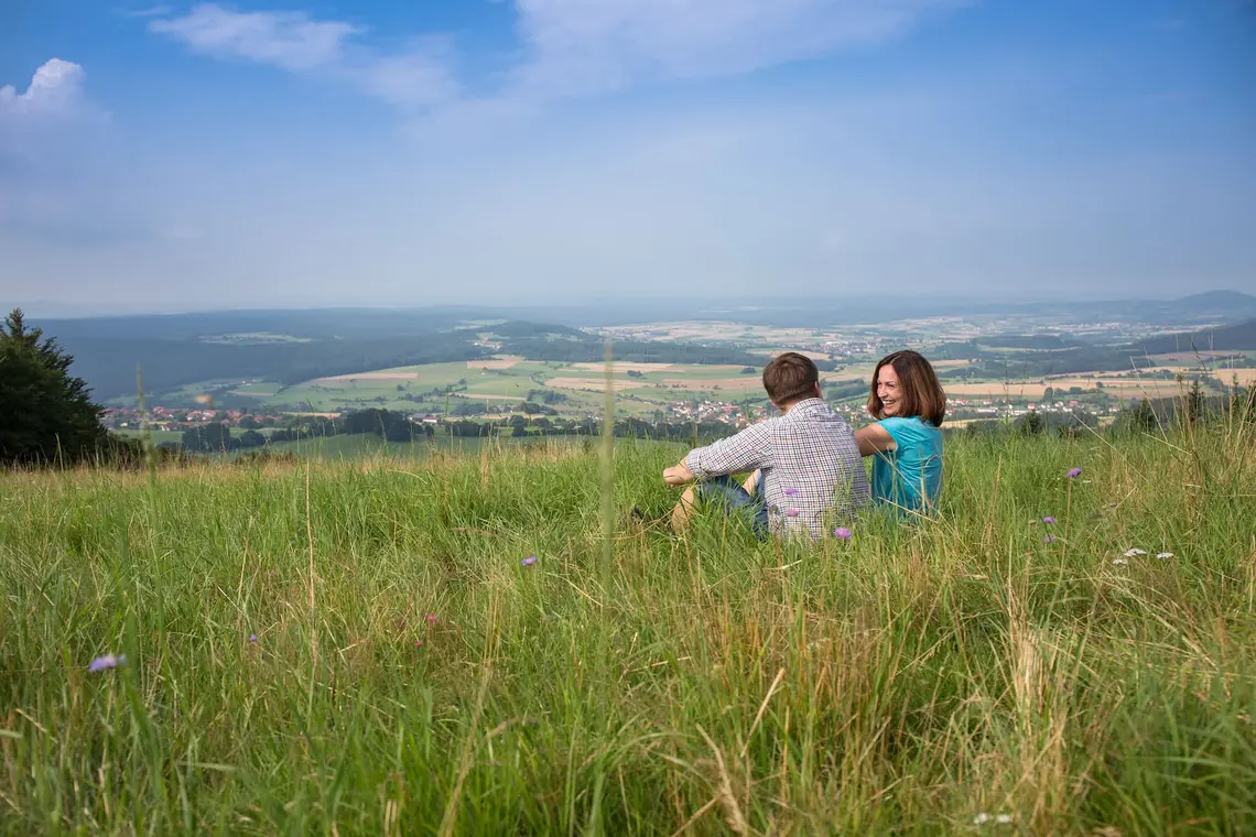 Ein Mann und eine Frau sitzen auf einer großen Wiese mit Blick in die Ferne