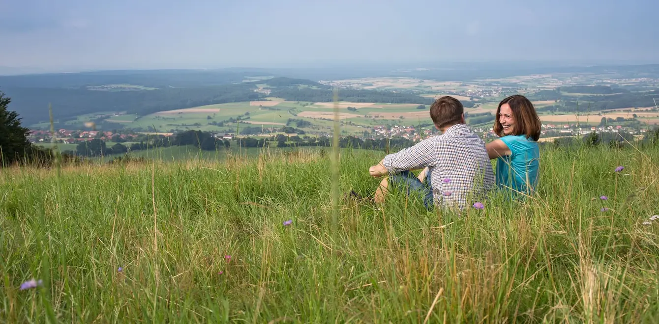 Ein Mann und eine Frau sitzen auf einer großen Wiese mit Blick in die Ferne