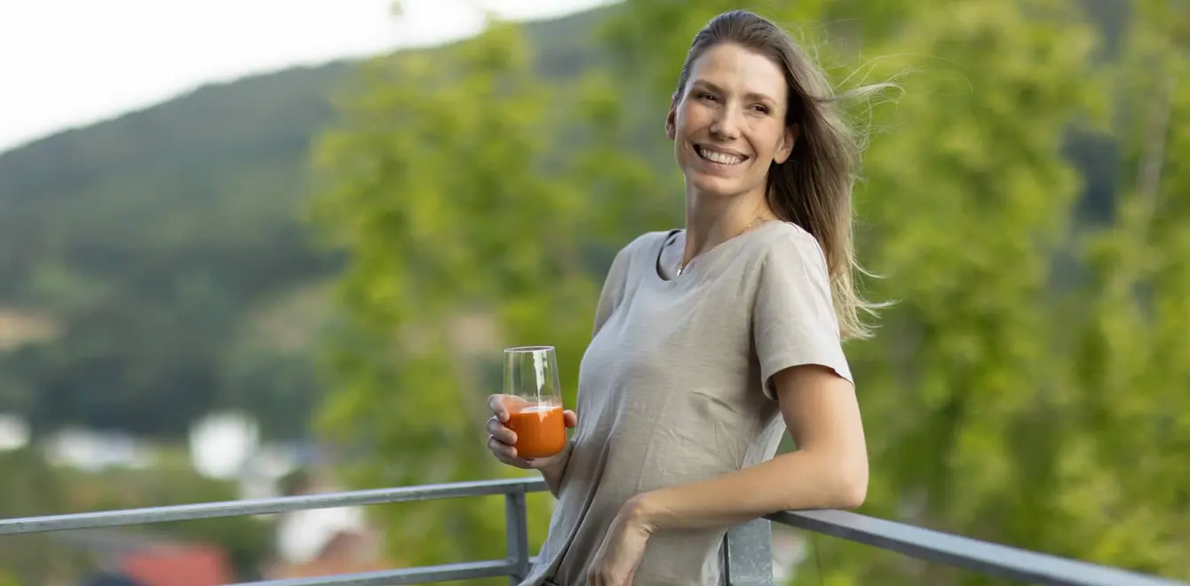 Eine Frau hält ein Glas in der Hand und lehnt sich rückwärts mit einem Arm an ein Balkongeländer