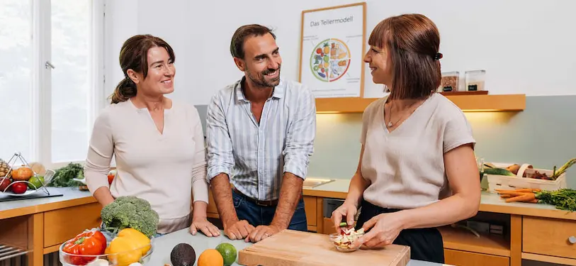 Zwei Frauen und ein Mann stehen in einer Küche und bereiten Gemüse zu