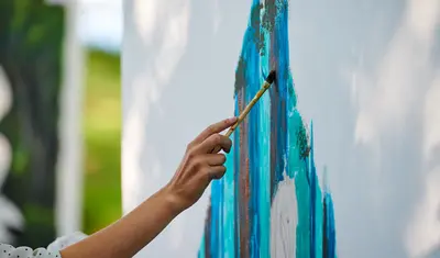 Eine Frau malt mit einem Pinsel eine blaue Fläche auf einer weißen Wand