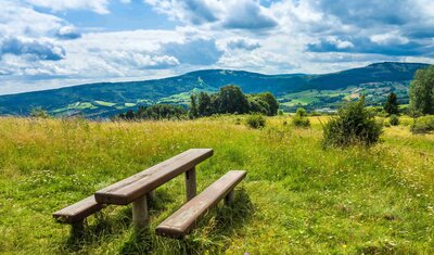Zwei Bänke und ein Tisch auf einer Wiese in der Rhön, mit Bergen im Hintergrund