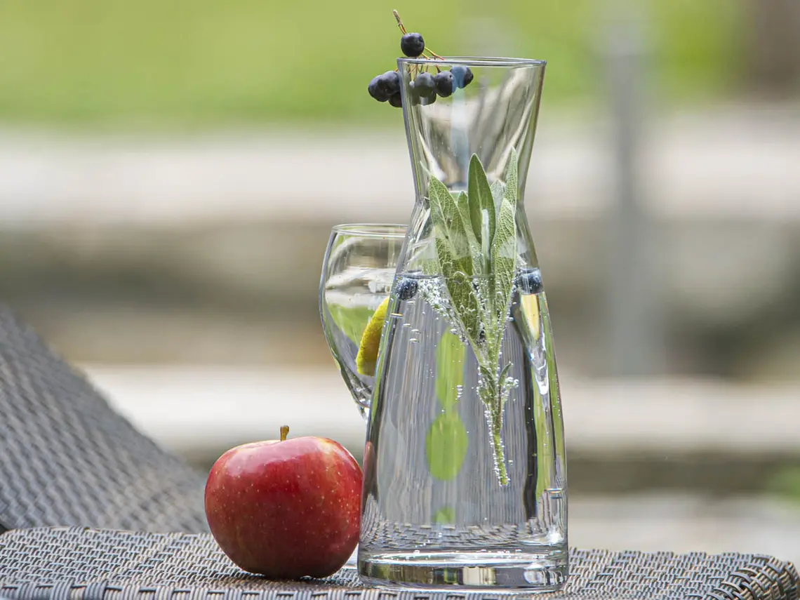 Roter Apfel liegt neben einer Glaskaraffe auf einem Outdoor-Tisch
