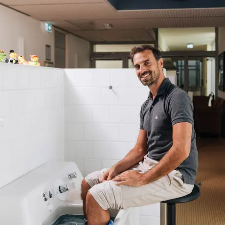 Ein Mann sitzt vor einem Wasserbecken, wo er die Füße hineinhält, auf einem Stuhl