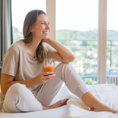 Frau sitzt auf einem Bett in der Dr. von Weckbecker Klinik mit einem Saft in der Hand
