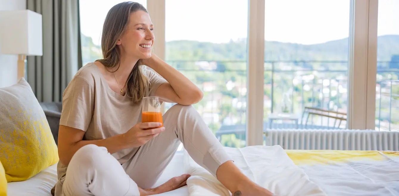 Frau sitzt auf einem Bett in der Dr. von Weckbecker Klinik mit einem Saft in der Hand
