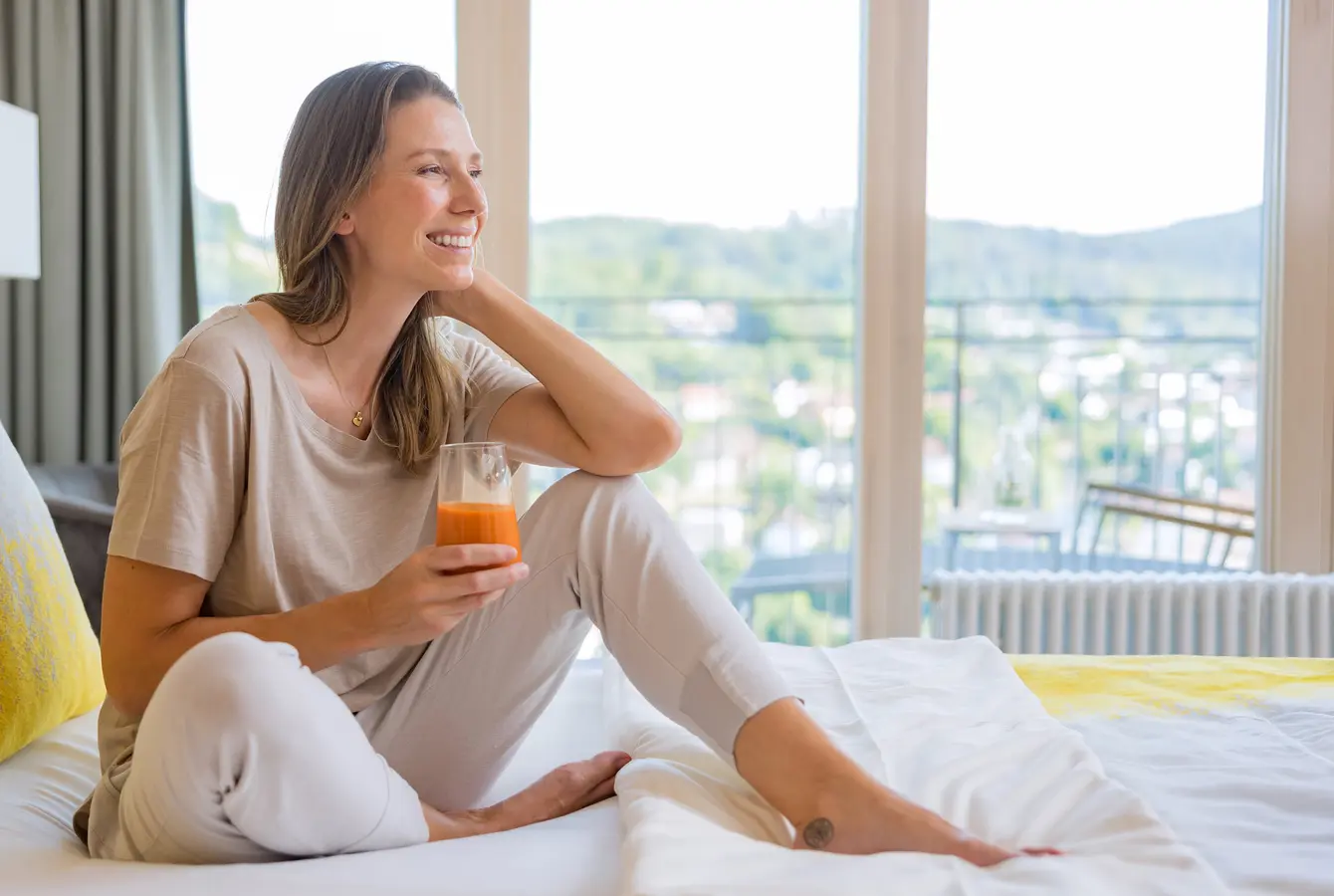 Frau sitzt auf einem Bett in der Dr. von Weckbecker Klinik mit einem Saft in der Hand
