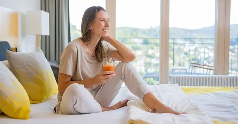Frau sitzt auf einem Bett in der Dr. von Weckbecker Klinik mit einem Saft in der Hand
