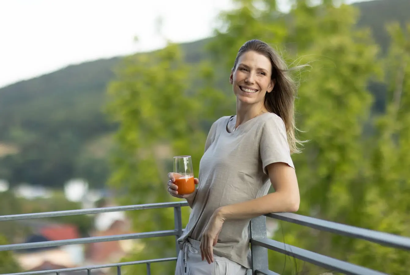 Eine Frau hält ein Glas in der Hand und lehnt sich rückwärts mit einem Arm an ein Balkongeländer