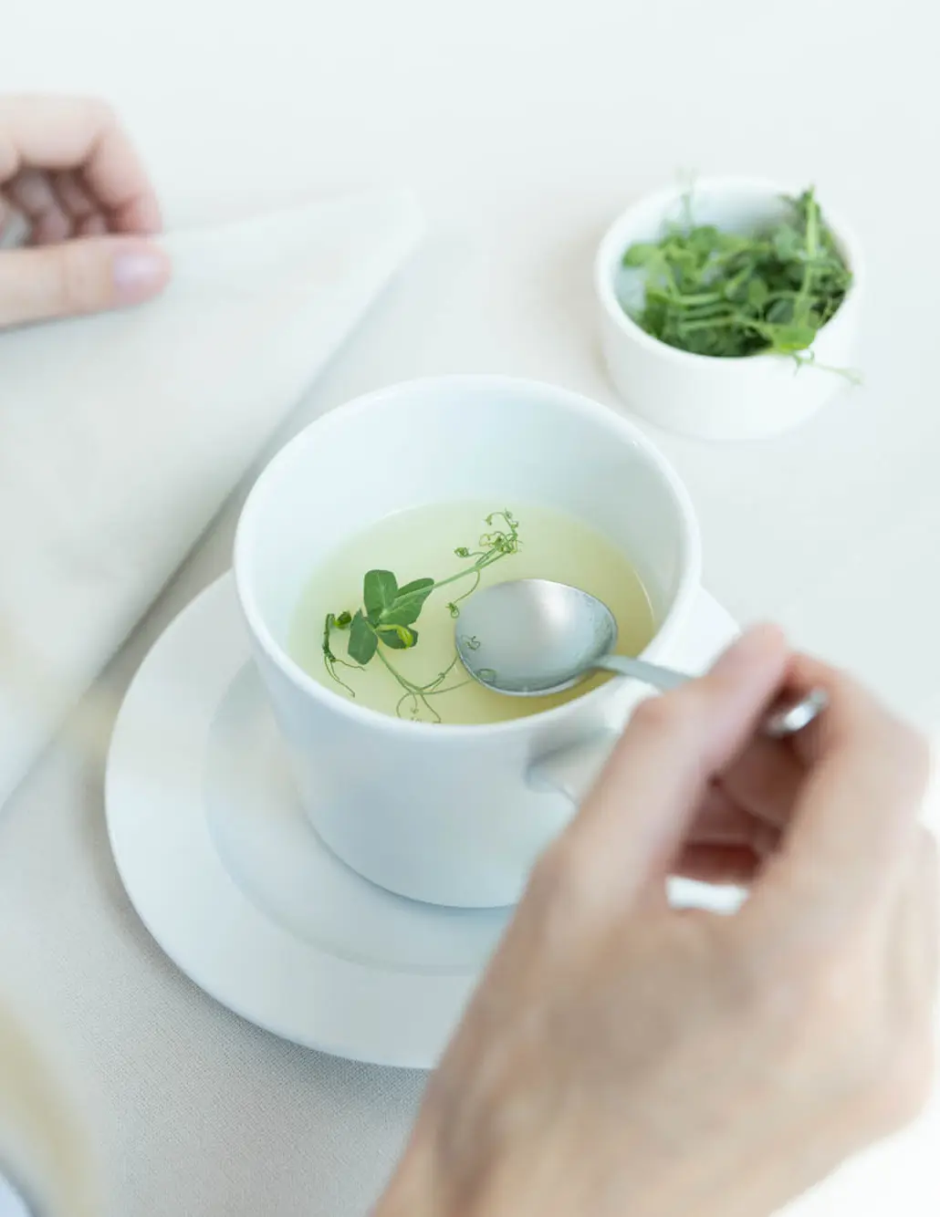 Eine Brühe in einer weißen Tasse. Der Tisch, das Geschirr und die Serviette sind weiß