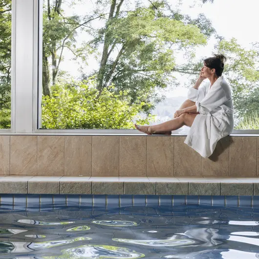 Eine Frau sitztz im Bademantel auf einer breiten Fensterbank im Schwimmbad der Klinik von Weckbecker