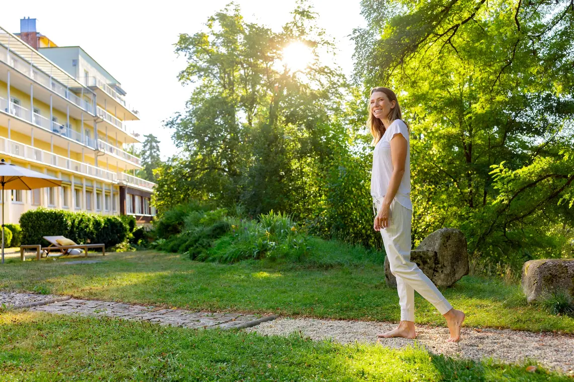 Eine Frau geht barfuß durch die Grünflächen der Weckbecker Klinik auf einem Fußweg