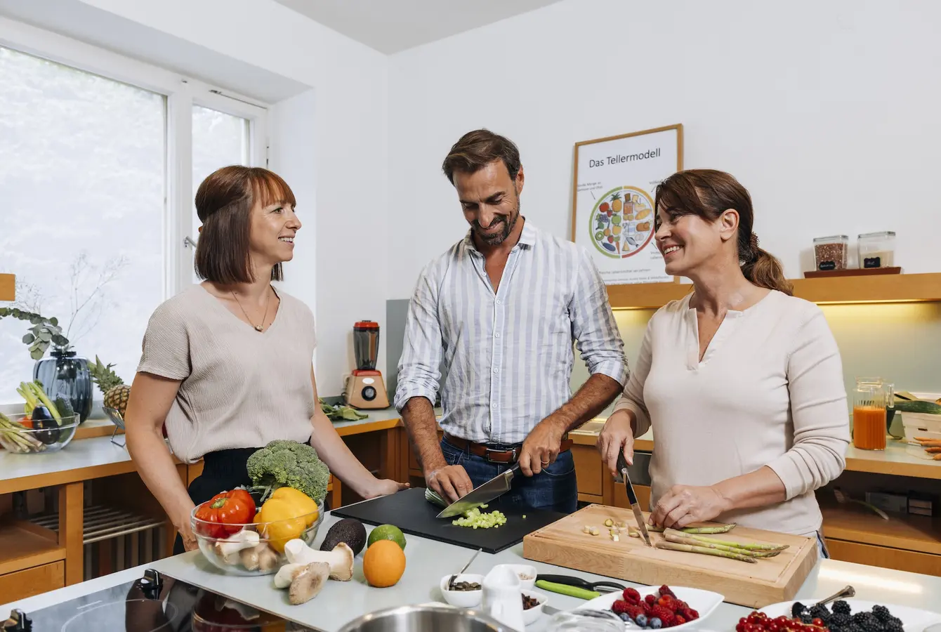 Zwei Frauen und ein Mann stehen in der Küche und bereiten Essen zu